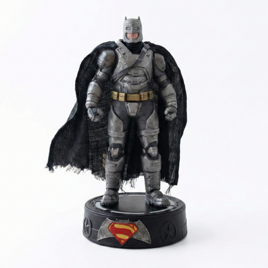 22cm Armored Batman action figure with weathered metallic suit, tattered fabric cape, and glowing BvS LED base for Krishna Toyverse India.